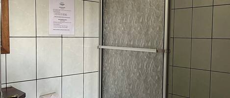 Un baño con inodoro, cabina de ducha y un cubo de basura azul.