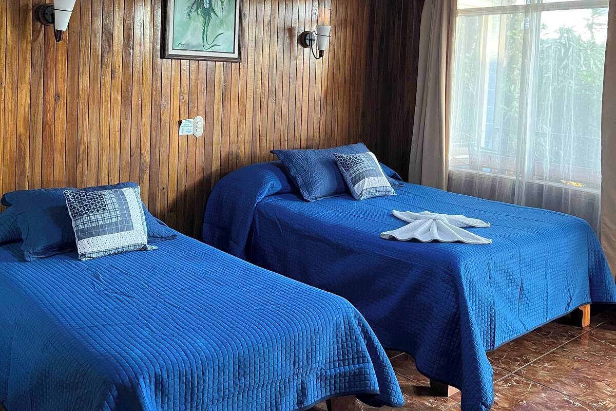 Une chambre avec deux lits, des murs en bois, un ventilateur de plafond et une fenêtre avec des rideaux.