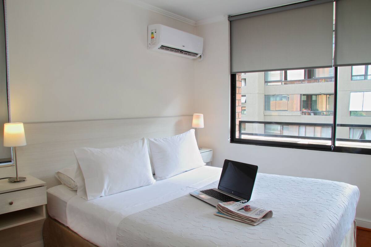 Ein Hotelzimmer mit Bett, Laptop und Fenster mit Blick auf Gebäude.