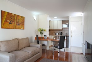 Una sala de estar con un sofá, un comedor con mesa y sillas, una cocina con gabinetes y electrodomésticos, y un televisor.