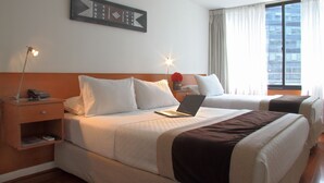 Ein Hotelzimmer mit zwei Betten, einem Laptop auf einem Bett, einem Nachttisch mit Lampe und einem gerahmten Bild an der Wand.