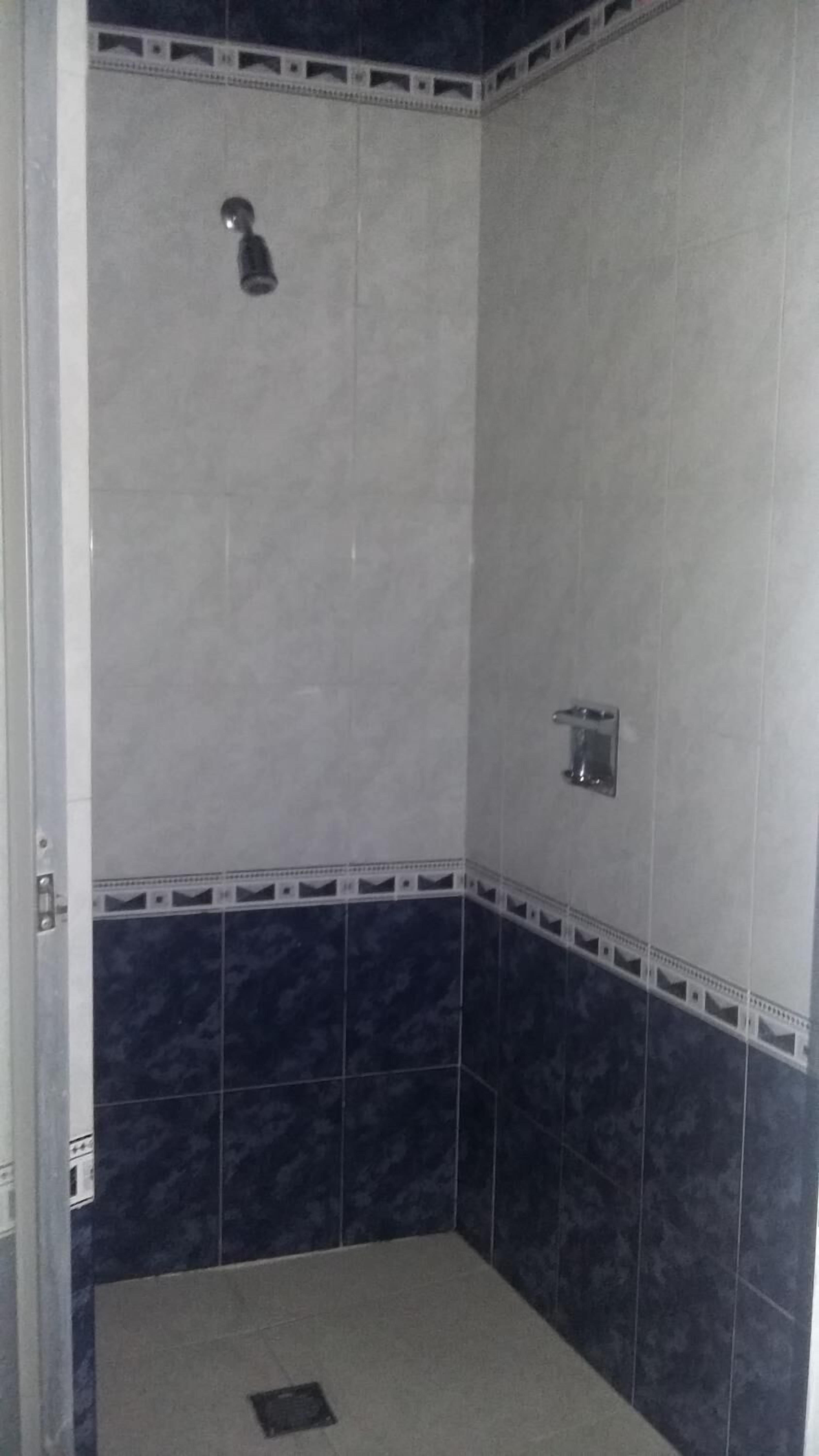 A small, tiled shower room with a single showerhead and a small shelf.