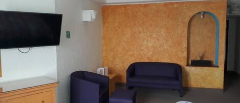 A hotel room with a bed, a dresser, a TV, a sofa, and a small table.