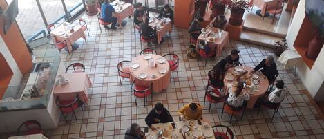 Un restaurant doté de plusieurs tables et chaises rondes, de grandes fenêtres et de plantes en pot.