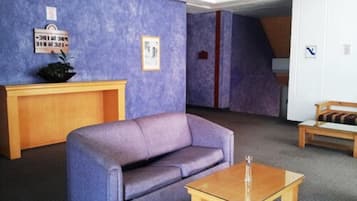 Una habitación con un sofá púrpura, una mesa de madera y un pequeño banco de madera. Hay un letrero en la pared y un cuadro enmarcado.
