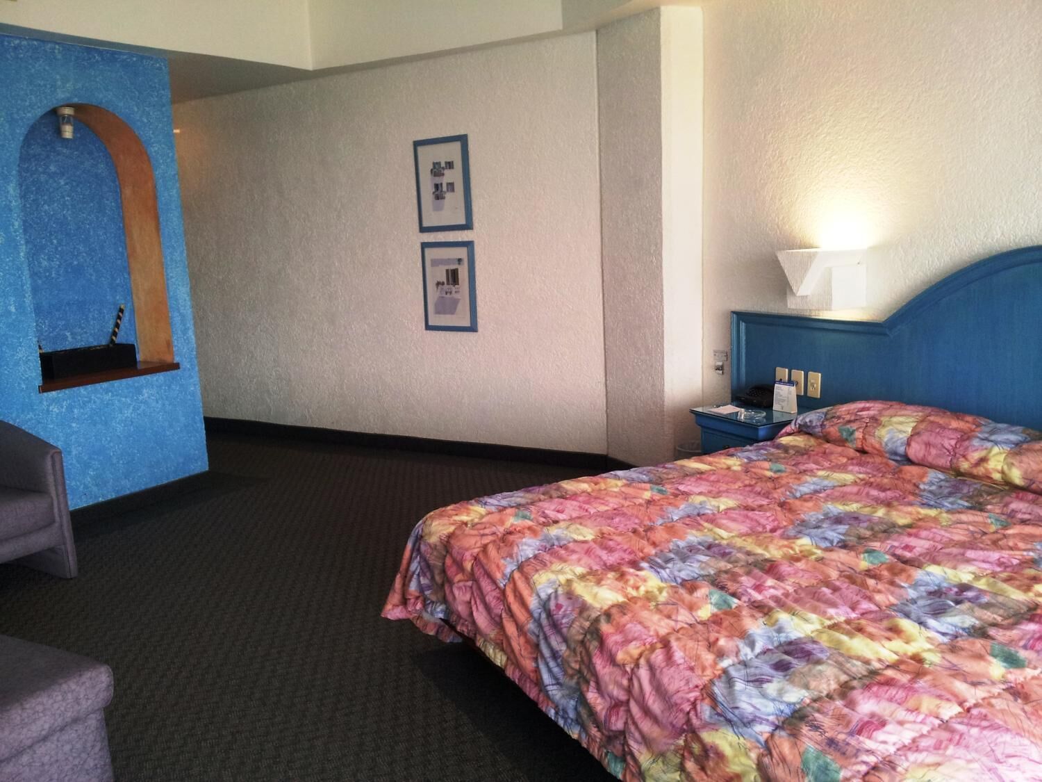 A hotel room with a bed, a desk, a chair, and a wall-mounted shelf.