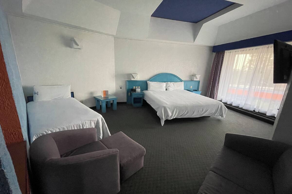 A hotel room with two beds, a sofa, a small table, and a TV.
