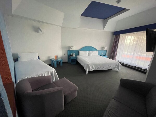 Habitación de hotel con dos camas, un sofá, una mesita y un televisor.