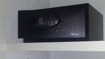 A black electronic device on a shelf, possibly a security system or intercom, with a white wall and a door with a towel hanging on it.