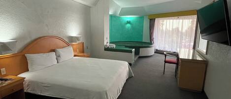 Una habitación de hotel con cama, escritorio, silla, televisor y pared verde.