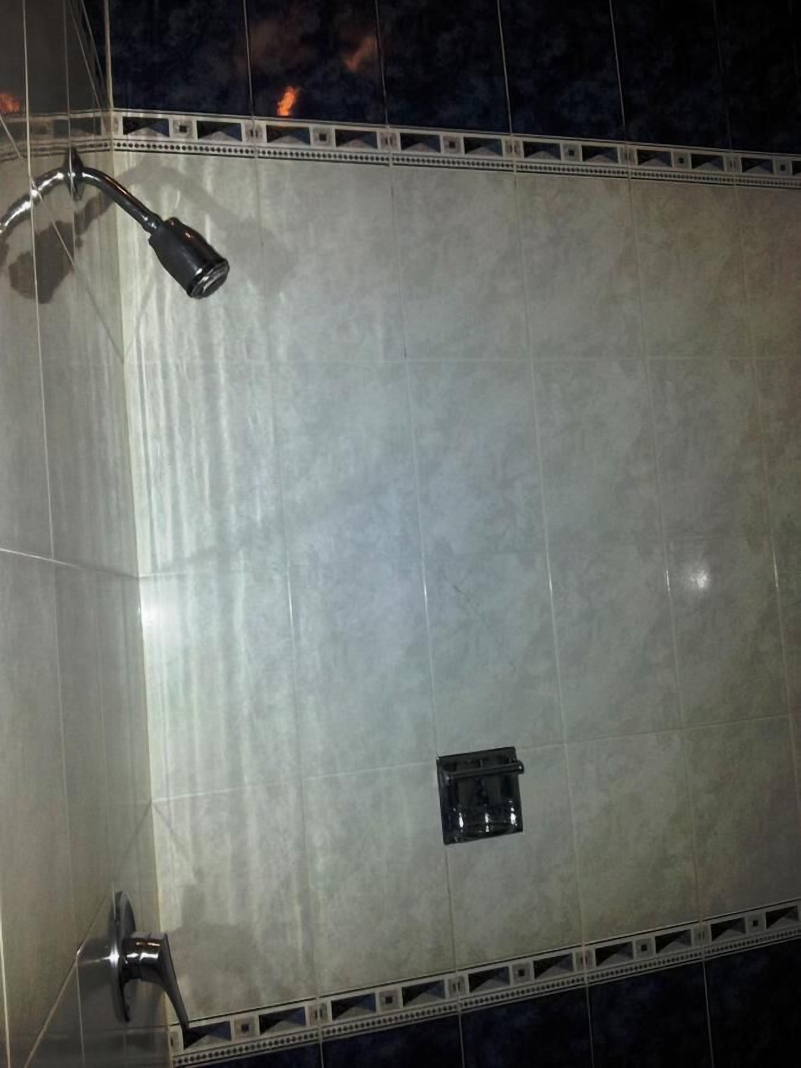 A bathroom with a large mirror, a showerhead, and a small sink.
