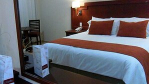 A hotel room with a large bed, a wooden headboard, a bedside table with a lamp, and a chair. - Hotel RS (Córdoba)
