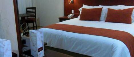 A hotel room with a large bed, a wooden headboard, a bedside table with a lamp, and a chair.