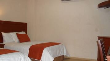 Ein Hotelzimmer mit zwei Betten, einem hölzernen Kopfteil, einem Schreibtisch und einer Klimaanlage an der Wand.