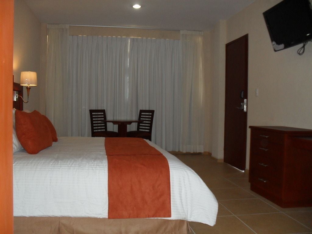 Una habitación de hotel con cama, escritorio, silla, televisor y armario.