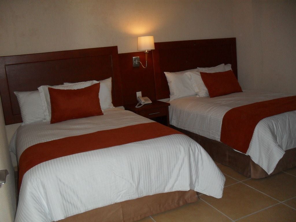 Dos camas dobles con ropa de cama blanca y roja, una mesita de noche con teléfono y una lámpara de pared.