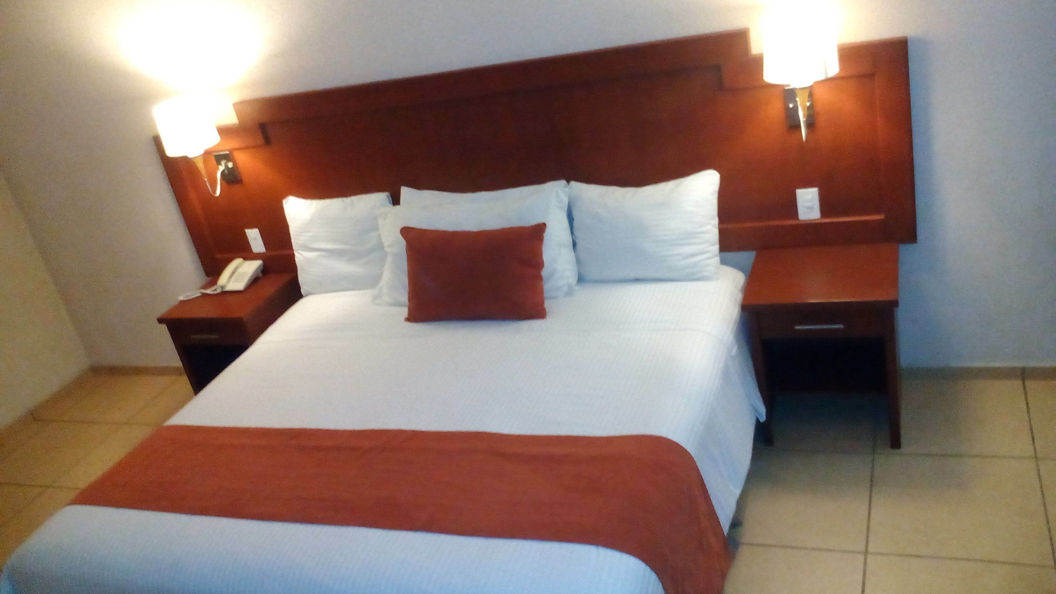 A hotel room with a large bed, two bedside tables, a wooden headboard, and wall-mounted lamps.
