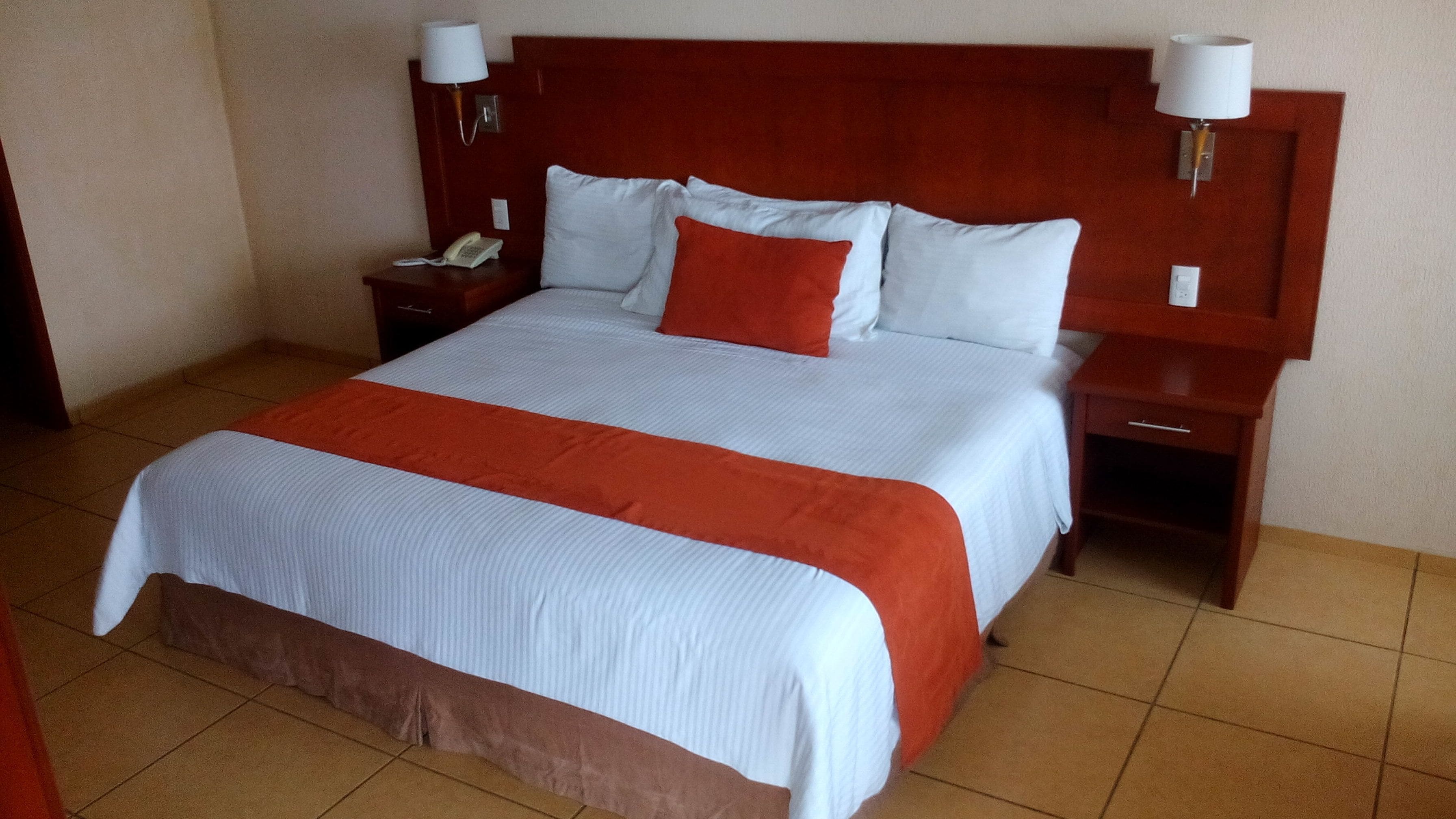 A hotel room with a large bed, two bedside tables, a nightstand, and a wall-mounted lamp.