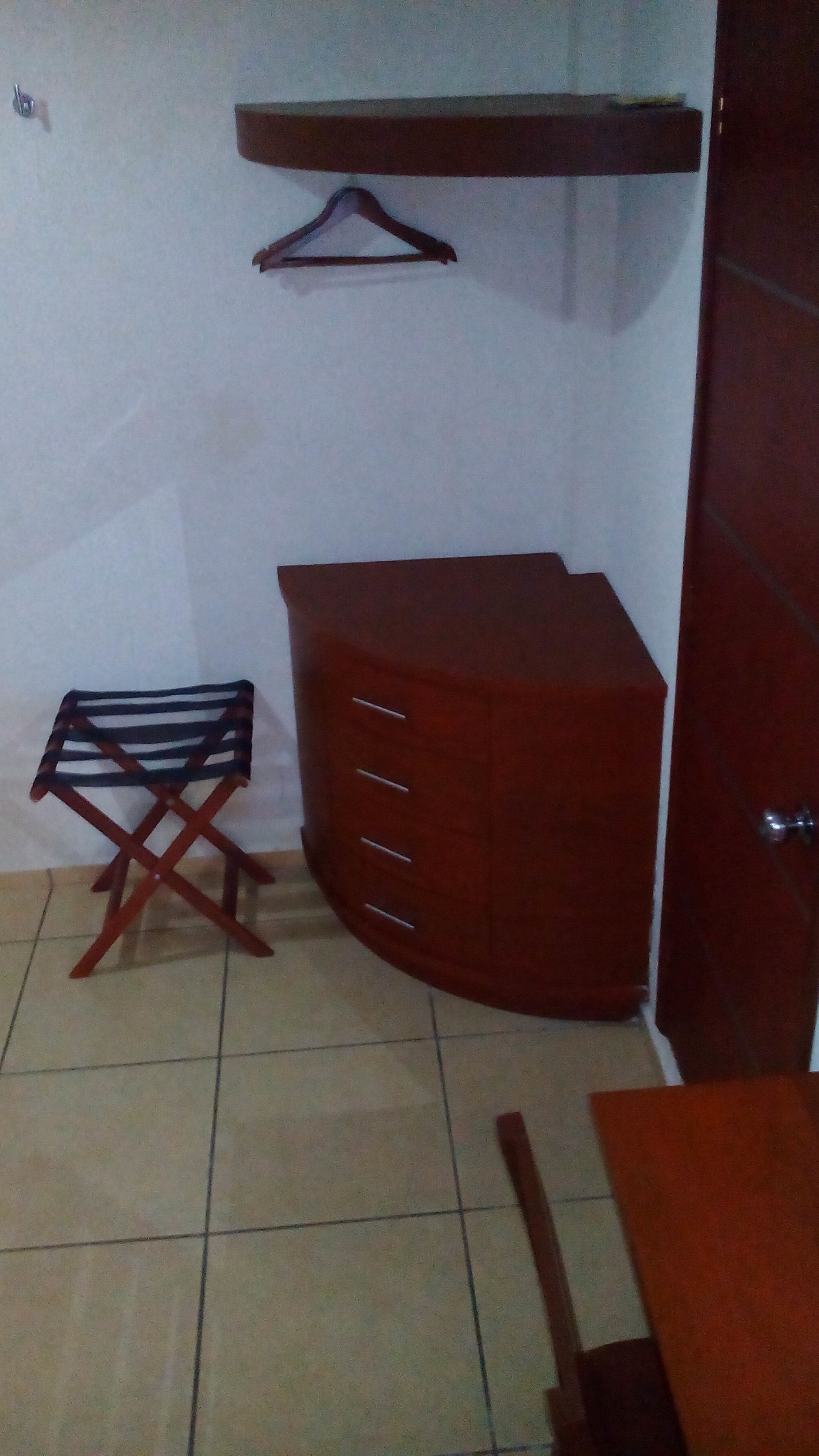 Ein Zimmer mit Fliesenboden, einem hölzernen Kommode mit Schubladen, einem kleinen Tisch und einem Stuhl.