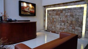A reception area with a wooden reception desk, a stone wall, and a framed artwork above the desk. - Hotel RS (Córdoba)