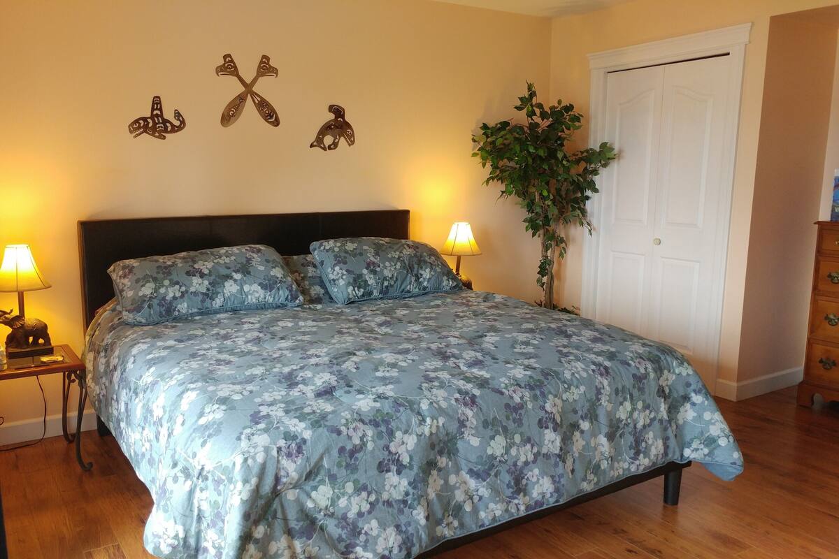 A bedroom with a floral bedspread, two bedside lamps, a nightstand with a lamp, a wooden dresser, and a door.