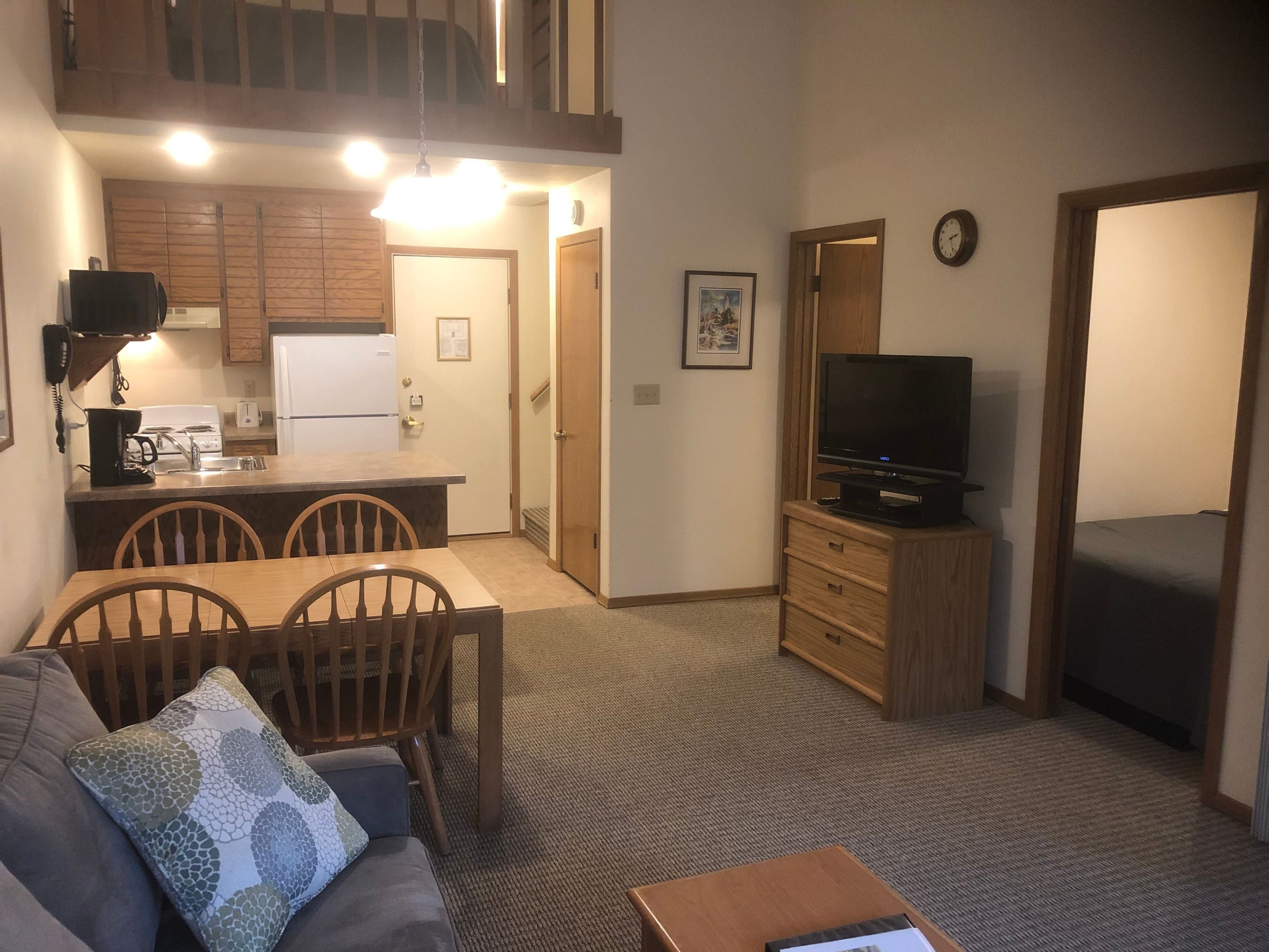 A compact living space with a kitchenette, a dining area, a television, and a sofa.
