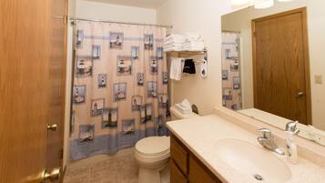 Un baño con cortina de ducha decorada con diseños de faros, un inodoro, un lavabo con espejo y toallas ordenadas.