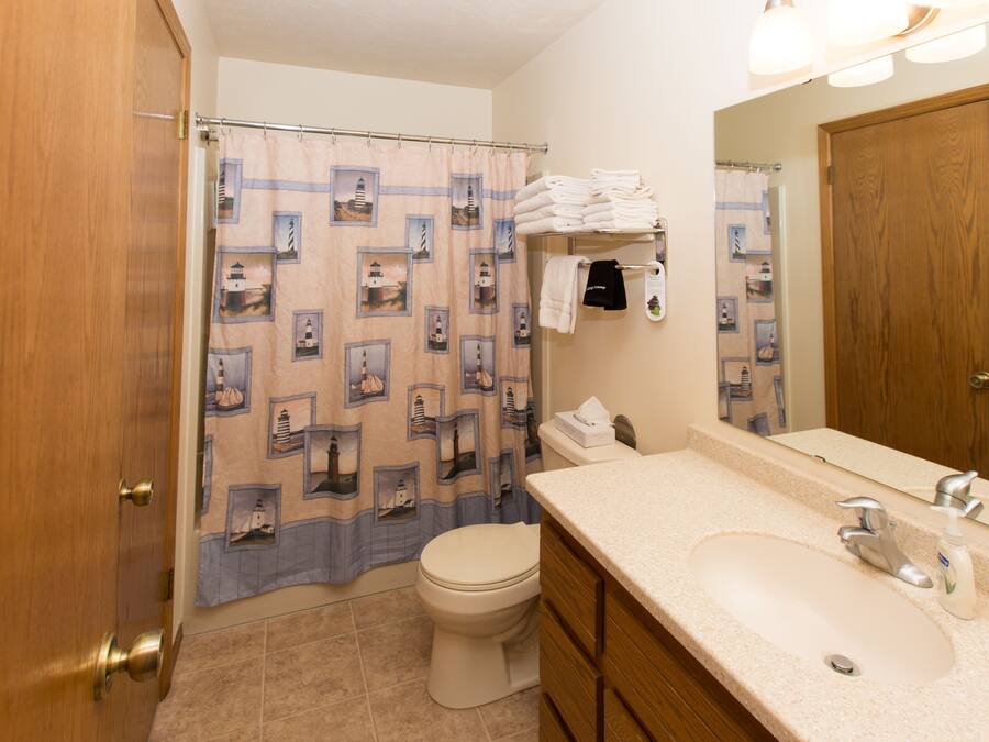 Un baño con cortina de ducha decorada con diseños de faros, un inodoro, un lavabo con espejo y toallas ordenadas.
