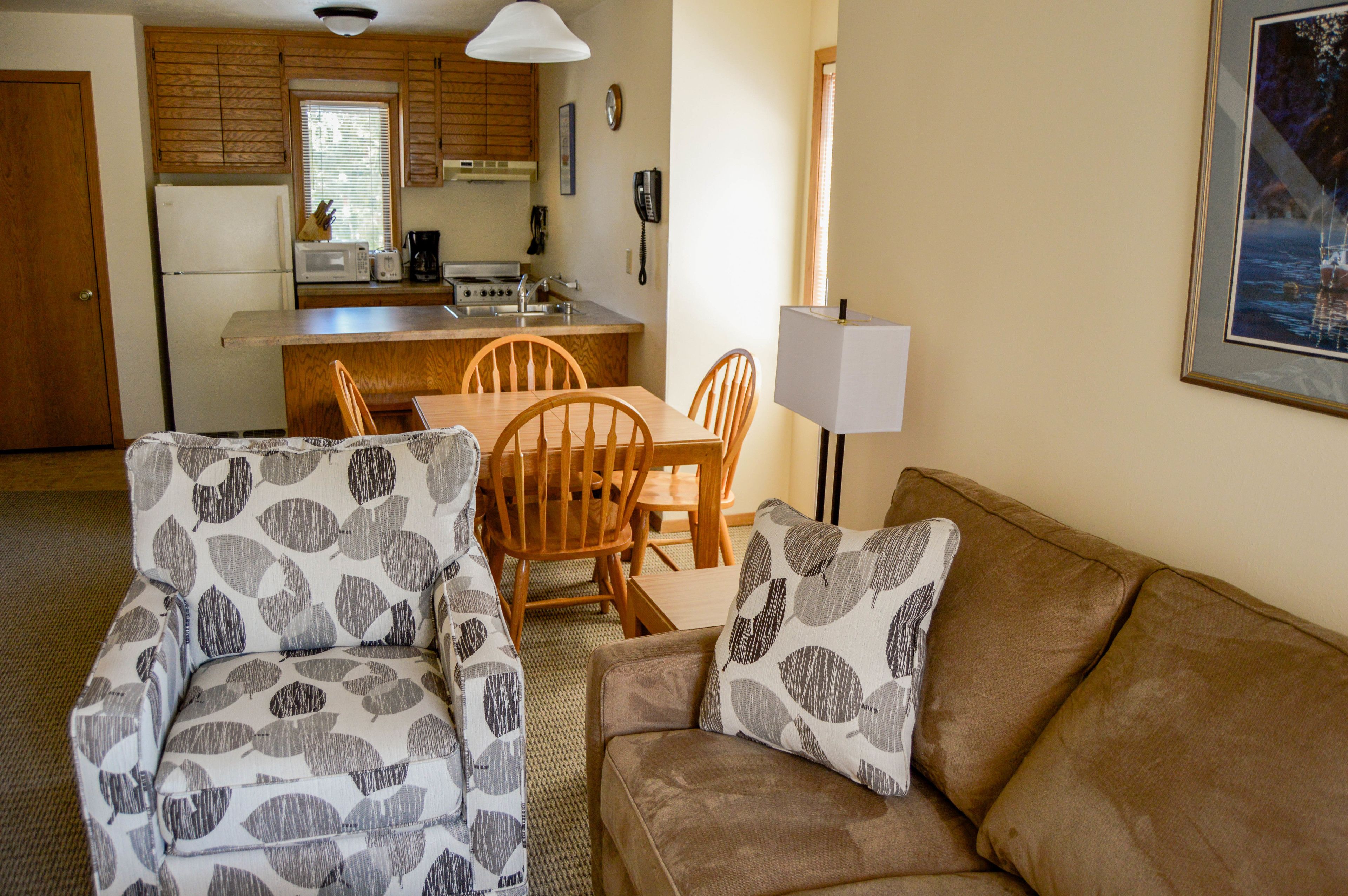 A compact living space with a kitchenette, a dining area, and a seating area with patterned armchairs and a sofa.