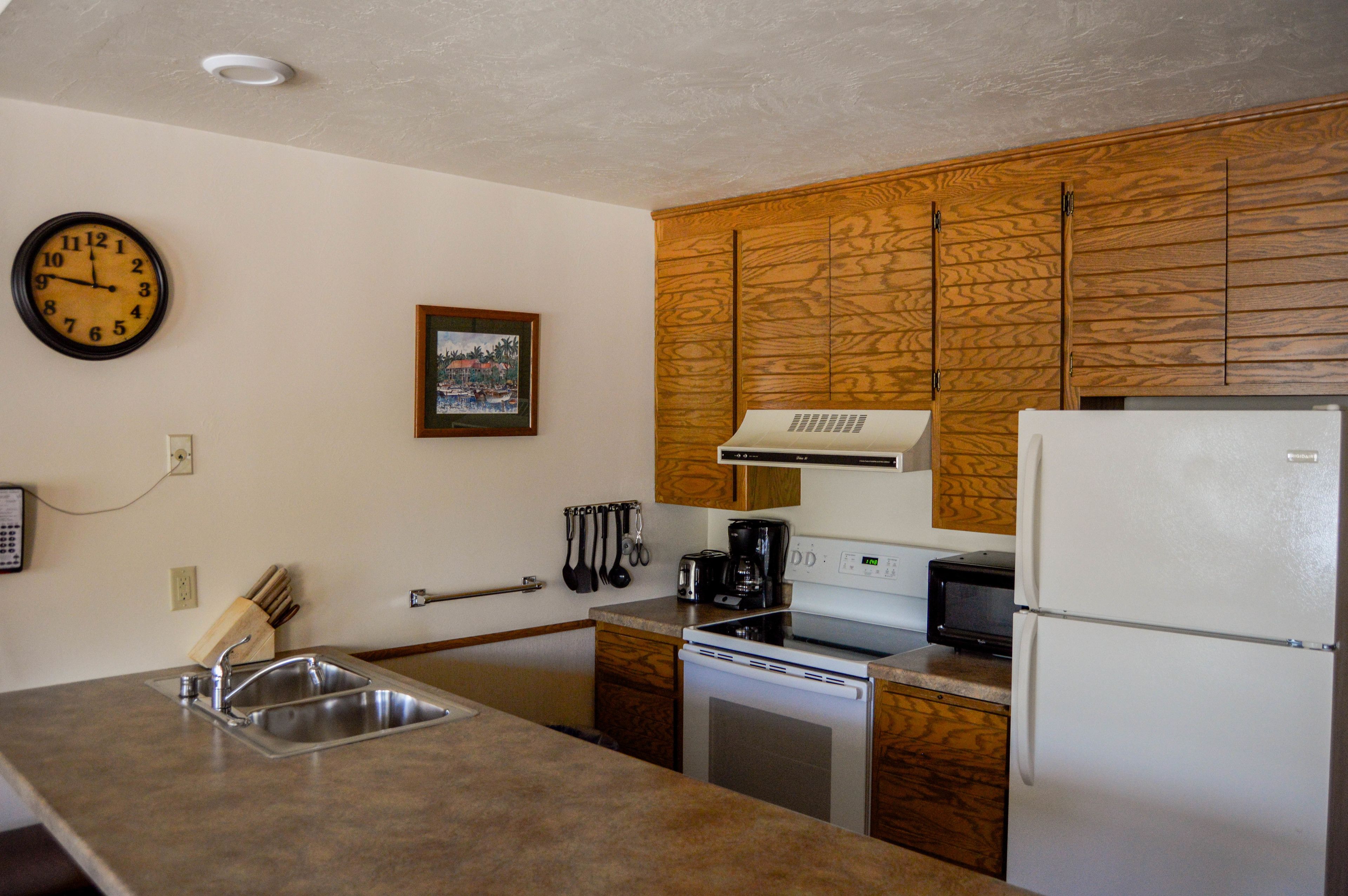 A kitchen with wooden cabinets, a stainless steel sink, a microwave, a stove, and a refrigerator.