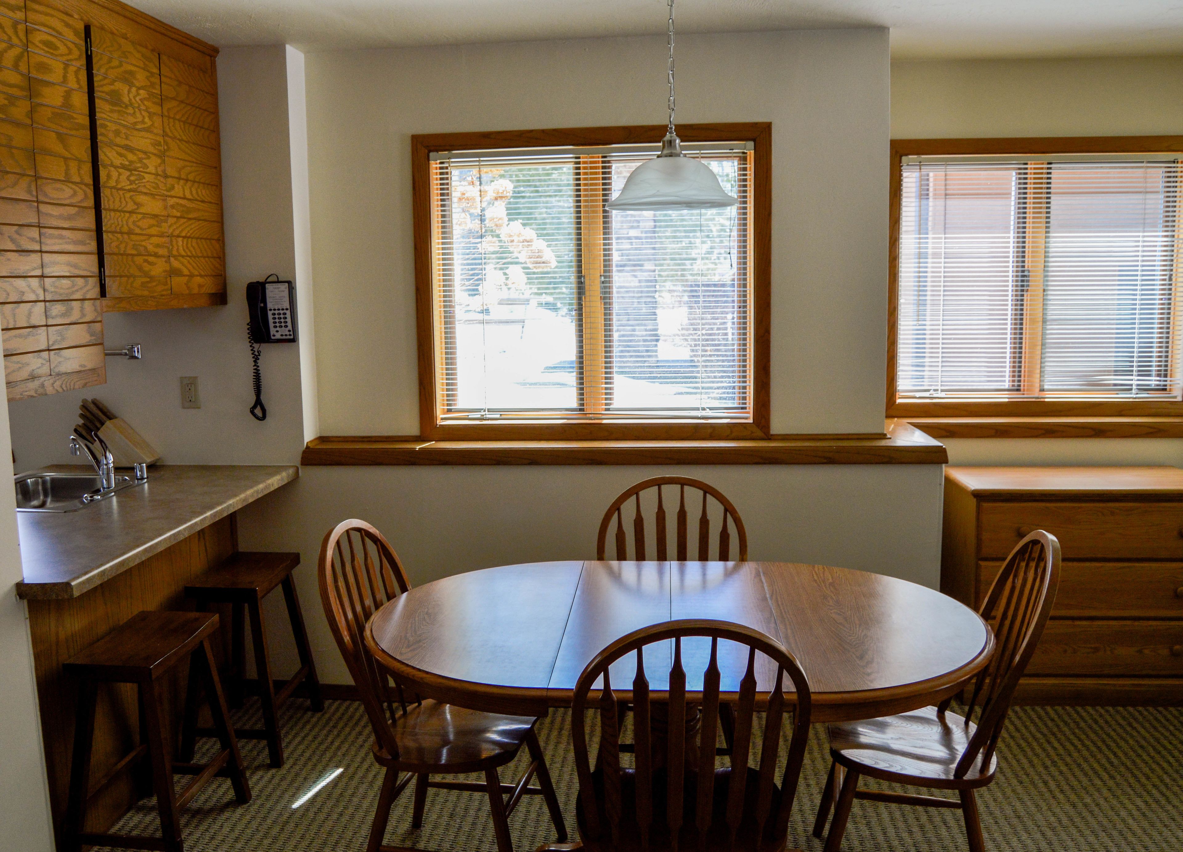 A kitchen with a wooden table, chairs, a sink, and a window with blinds.