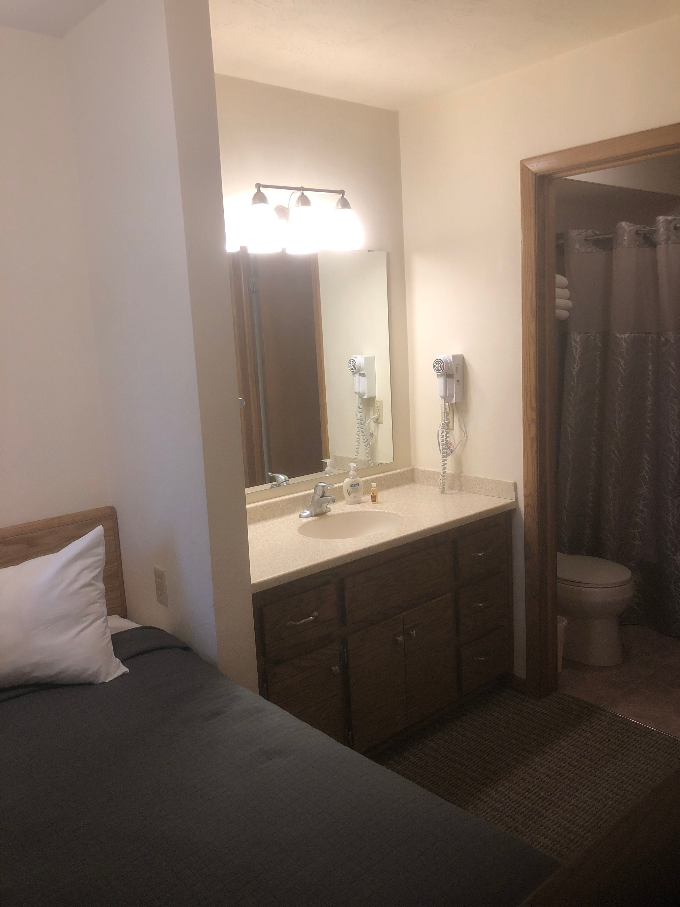 A hotel room with a bed, a bathroom with a shower curtain, a sink, and a mirror.