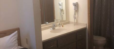 A hotel room with a bed, a bathroom with a shower curtain, a sink, and a mirror.