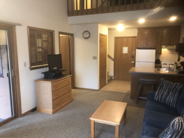 A compact living space with a kitchenette, a television on a wooden dresser, a sofa, and a small table. - The Landing Resort (Egg Harbor)