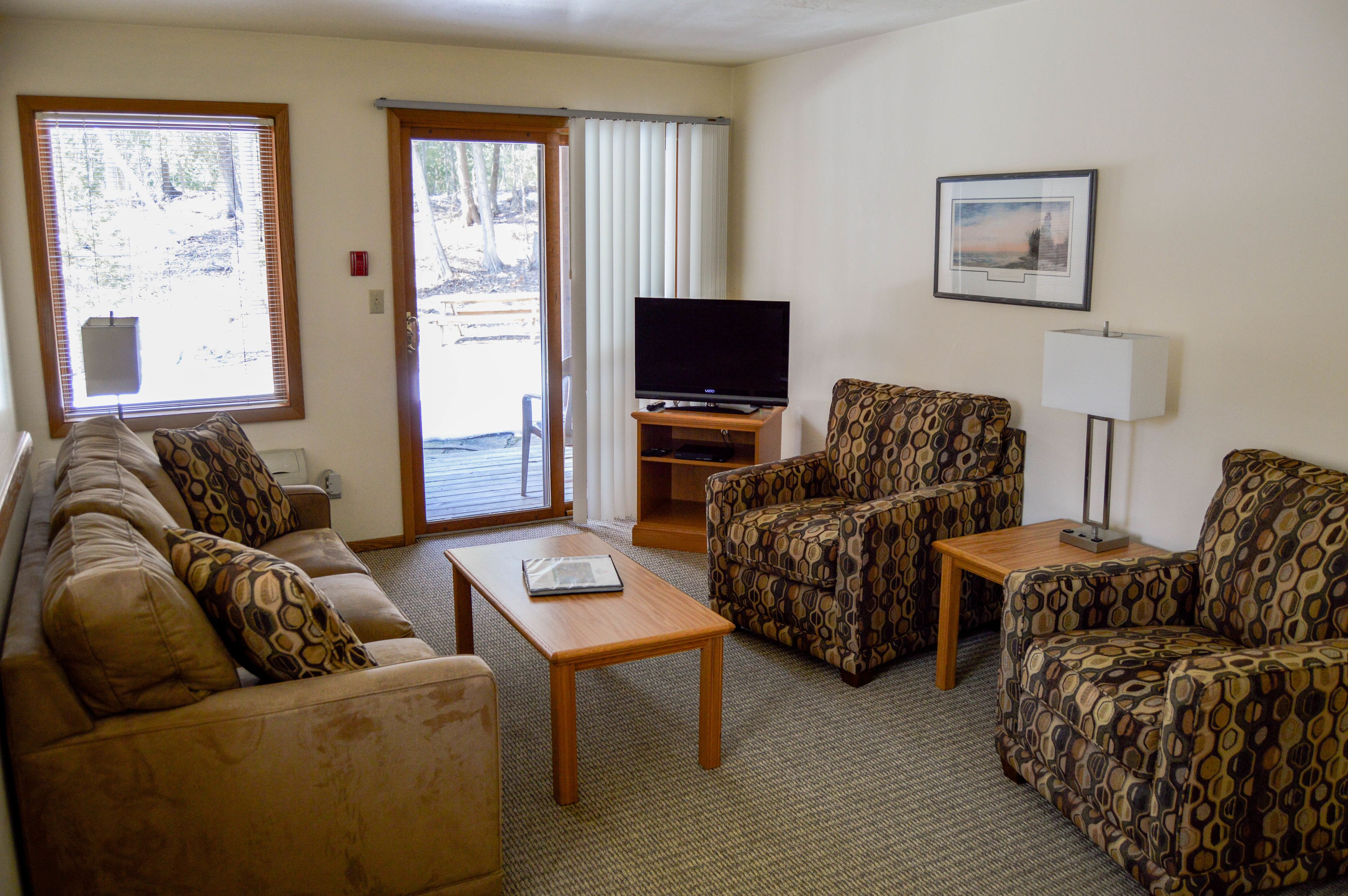 A living room with a sofa, armchair, coffee table, television, and a lamp.