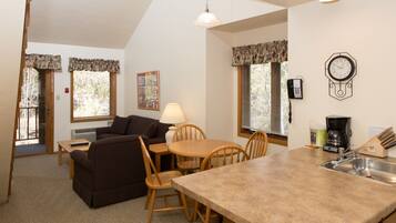 A kitchen with a wooden island, a dining table, and chairs. There is a clock on the wall and a window with blinds.