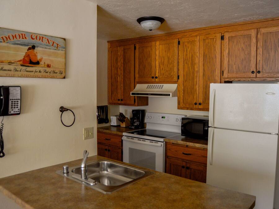 A kitchen with wooden cabinets, a stainless steel sink, a white refrigerator, and a stove.