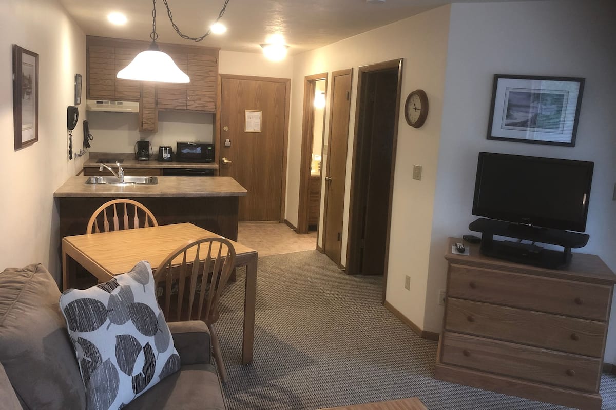 A compact living space with a kitchenette, a dining area, a TV, and a sofa.