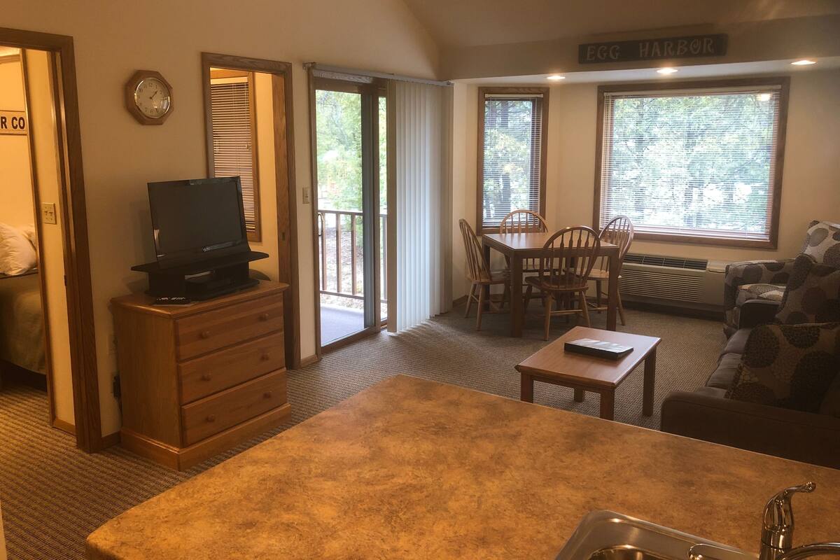 A cozy living room with a television, a dining table with chairs, a sofa, and a kitchen area with a sink.