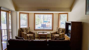 A living room with a brown couch, patterned armchairs, a wooden coffee table, and a television. There is a sign above the windows that reads "EGG HARBOR".