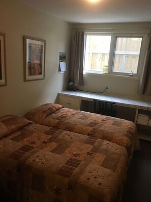 A bedroom with two beds, a desk, and a window with curtains. - Laura's Lodge (Saskatoon)