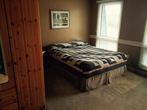 Un dormitorio con cama, un armario de madera, un cuadro enmarcado en la pared y una ventana con persianas.