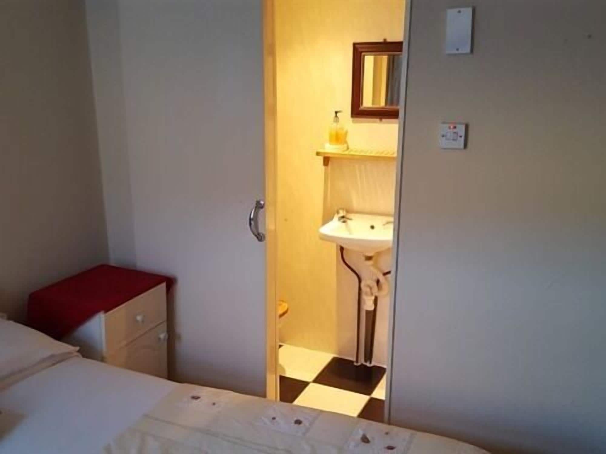 Una habitación pequeña y estrecha con una cama, un banco rojo, un lavamanos blanco y un espejo.