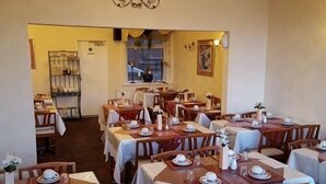 Un comedor con varias mesas dispuestas para el servicio, con manteles blancos y sillas de madera.