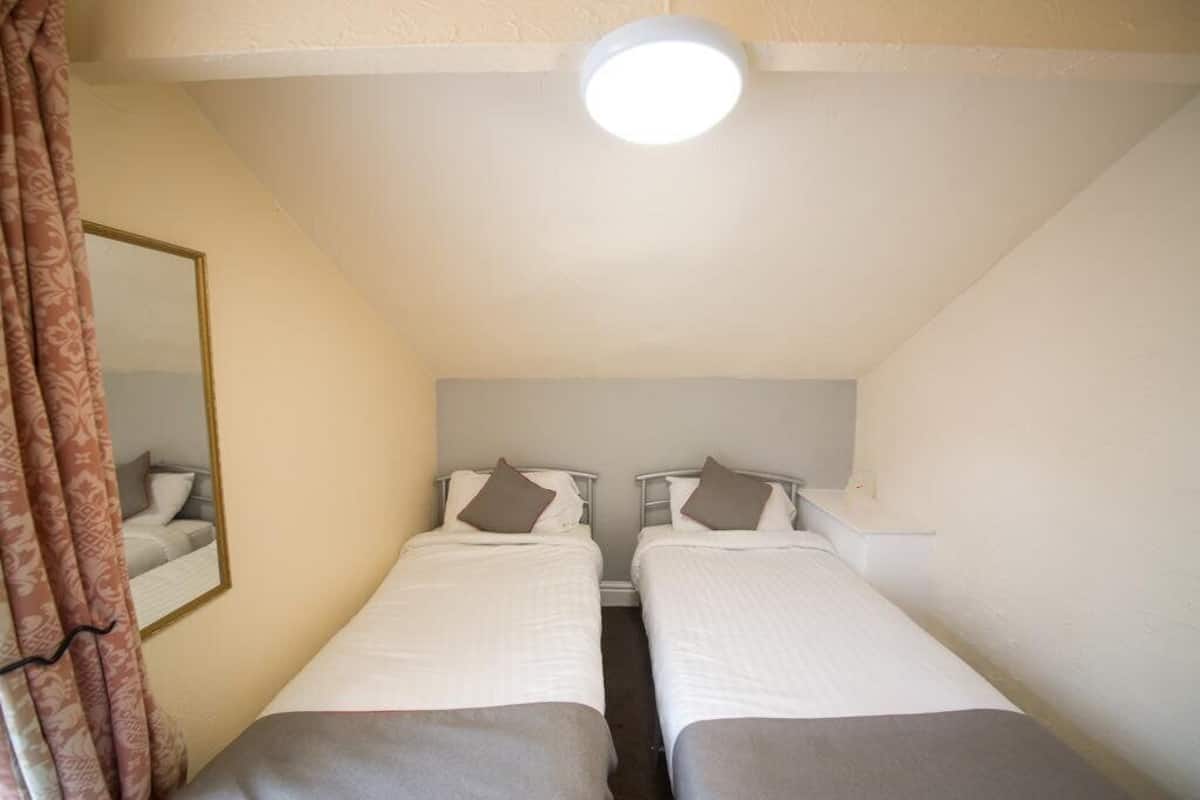 A small, well-lit room with two single beds, a bedside table, and a mirror on the left wall.
