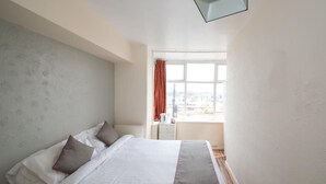 Una cama bien hecha con almohadas, una ventana con vistas y una mesita de noche con una lámpara.
