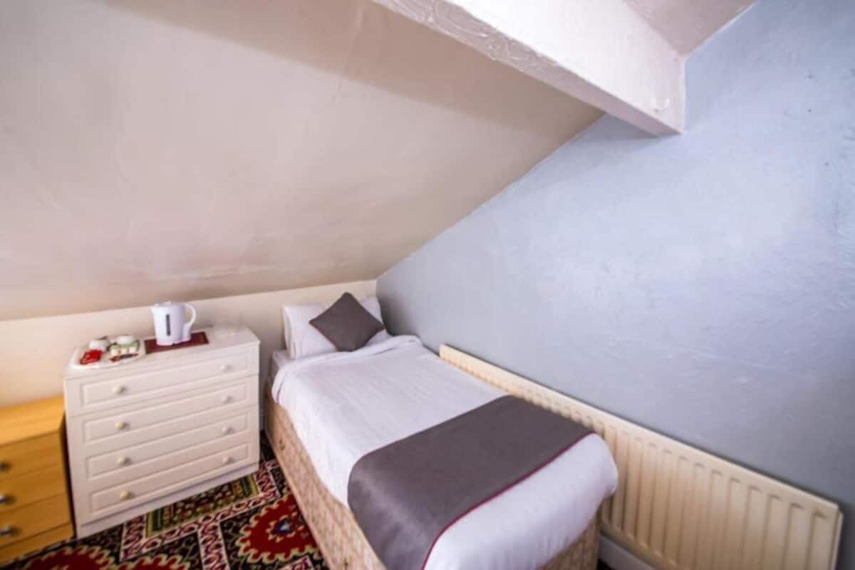 A small, neatly arranged bedroom with a single bed, a dresser, and a radiator.