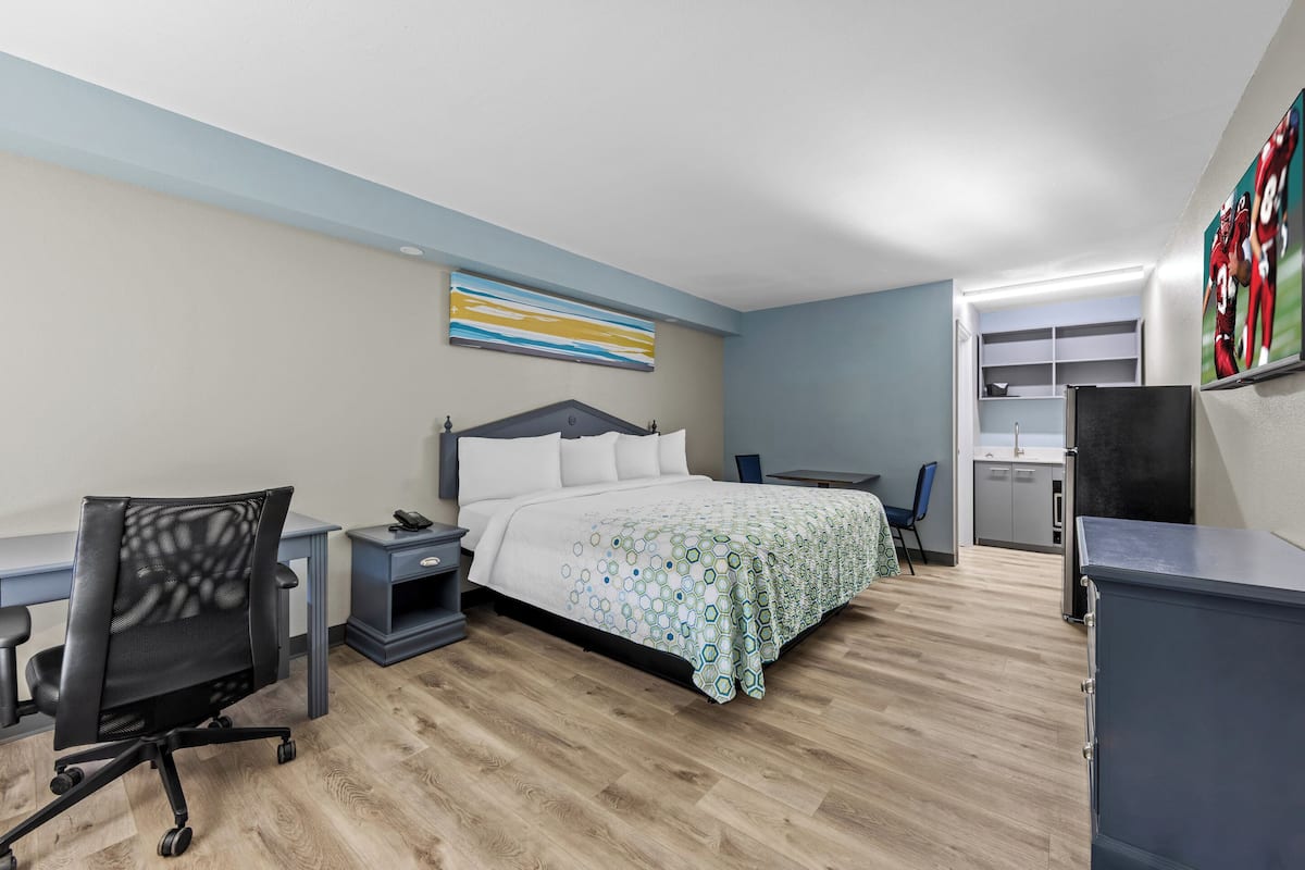 A hotel room with a bed, desk, chair, and kitchenette.