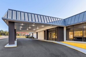 A modern building with a covered entrance, large windows, and a clear sky. - HomeTowne Studios by Red Roof Athens, TN (Athens)