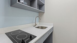 A modern kitchen with a built-in induction cooktop, a stainless steel sink, and grey cabinets. - HomeTowne Studios by Red Roof Athens, TN (Athens)